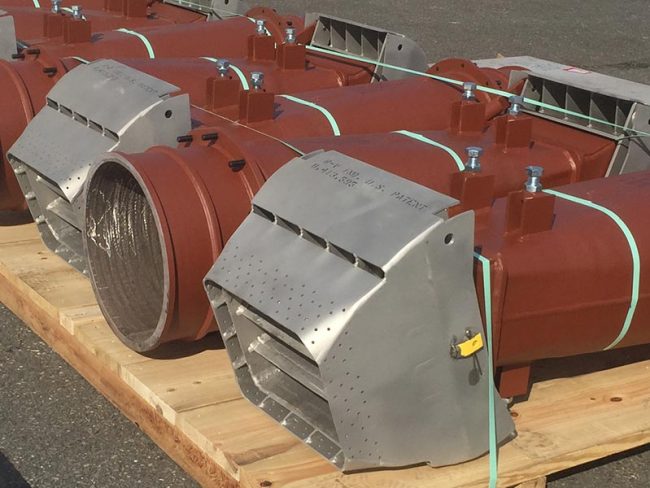 Several industrial coal nozzles with metal casings are arranged on a wooden pallet. The units are predominantly brown with silver-colored front covers, featuring multiple bolts and black seals. The front covers have multiple perforations.