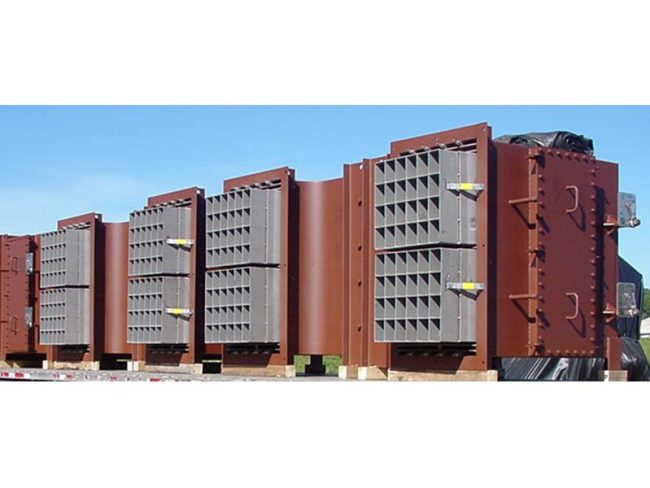 A row of large, industrial windboxes with a rust-colored exterior, grey paneling, and multiple bolted sections, all mounted on wooden pallets and situated outdoors under a clear sky.
